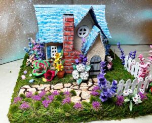 Cream-colored Easter house with blue shingles and many flowers surrounding