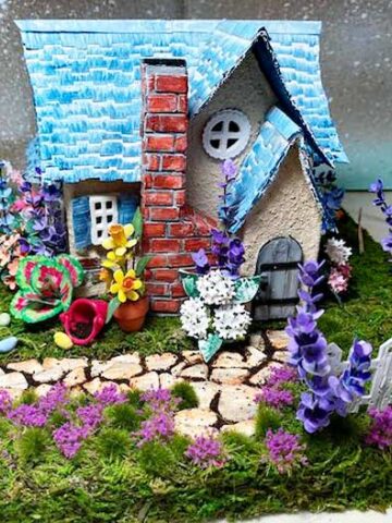 Cream-colored Easter house with blue shingles and many flowers surrounding