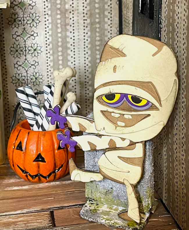 paper figure dressed as a mummy in front a pumpkin in a dollhouse
