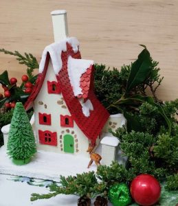 Among holiday greenery sits miniature holiday paper house