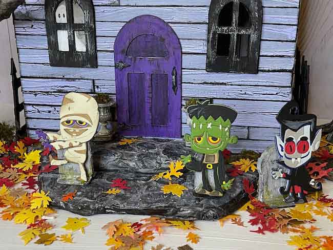 Colorful Halloween paper figures in front of purple dollhouse