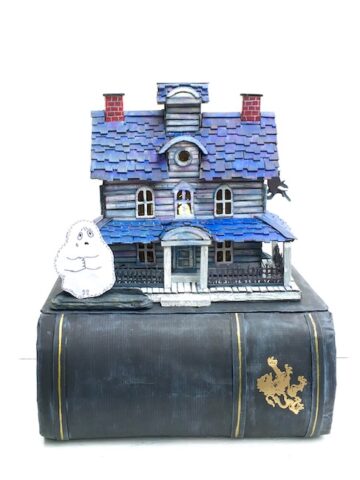 Cardboard house with blue roof and a ghost on a book