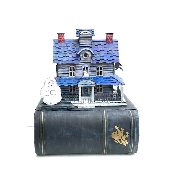 Cardboard house with blue roof and a ghost on a book