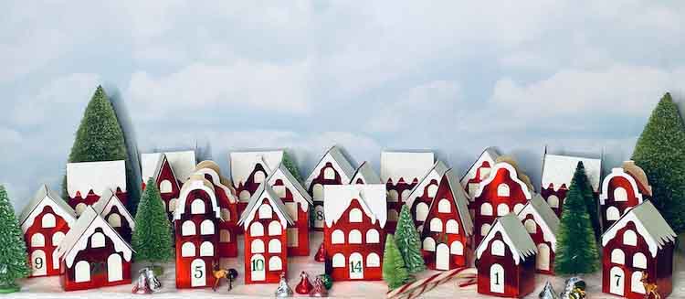 Red foil paper houses with white glitter paper trim surrounded by green bottlebrush trees with clouds in the background