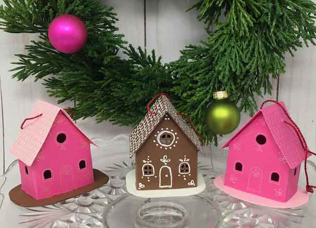 3 paper houses - 2 pink and one brown in front of a Christmas wreath