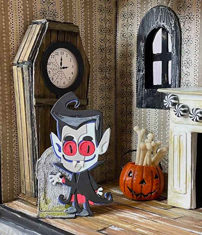 Vampire paper figure in front of paper coffin clock